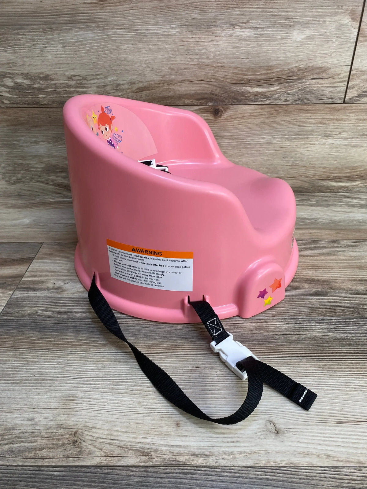 Three-quarter view of pink 15-inch Cocomelon children’s floor seat showing molded high back, safety buckle strap on wood floor
