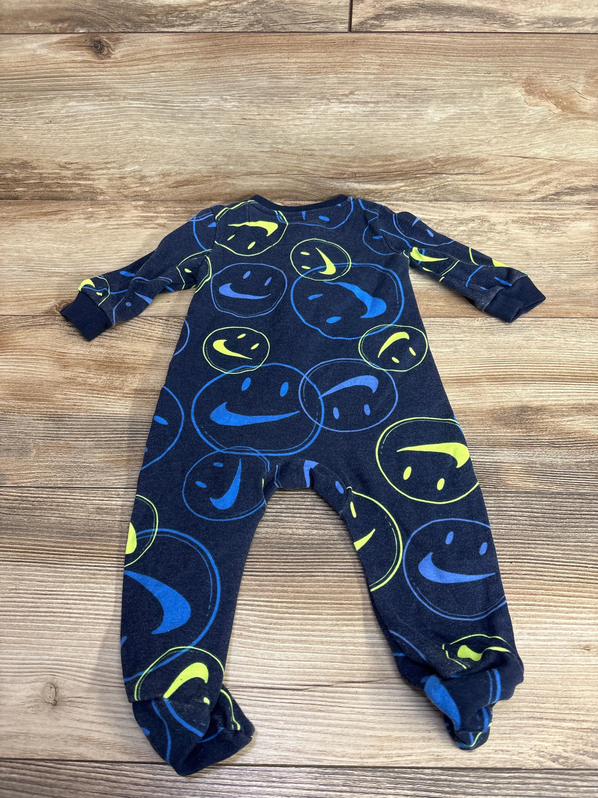 Navy blue baby sleeper with yellow and blue smiley face print on wood background