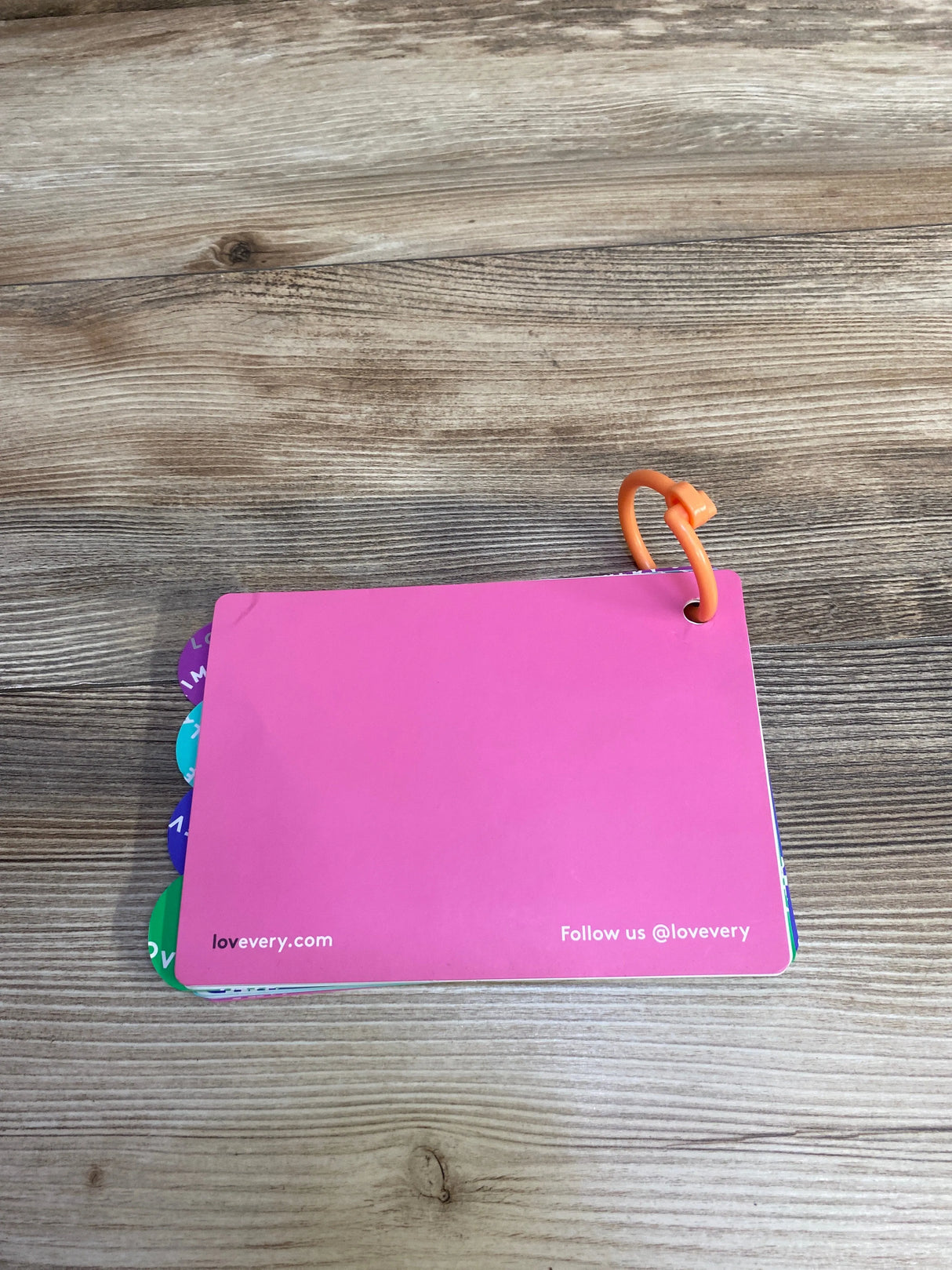 Pink flashcard with tabs on wooden surface, orange ring binding, lovevery.com branding