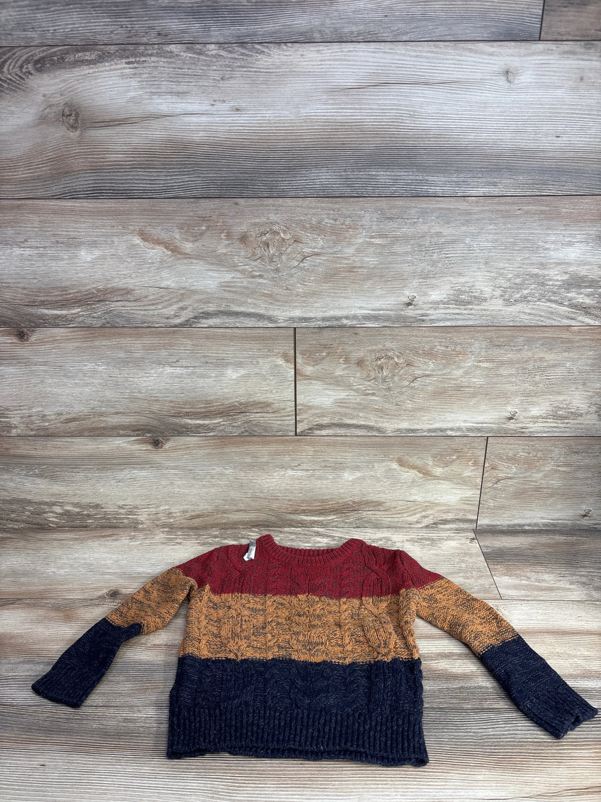 Kids cable knit sweater with red, mustard, and navy color blocks on wood background