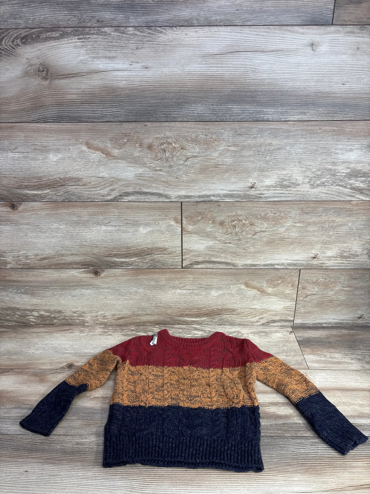 Kids cable knit sweater with red, mustard, and navy color blocks on wood background