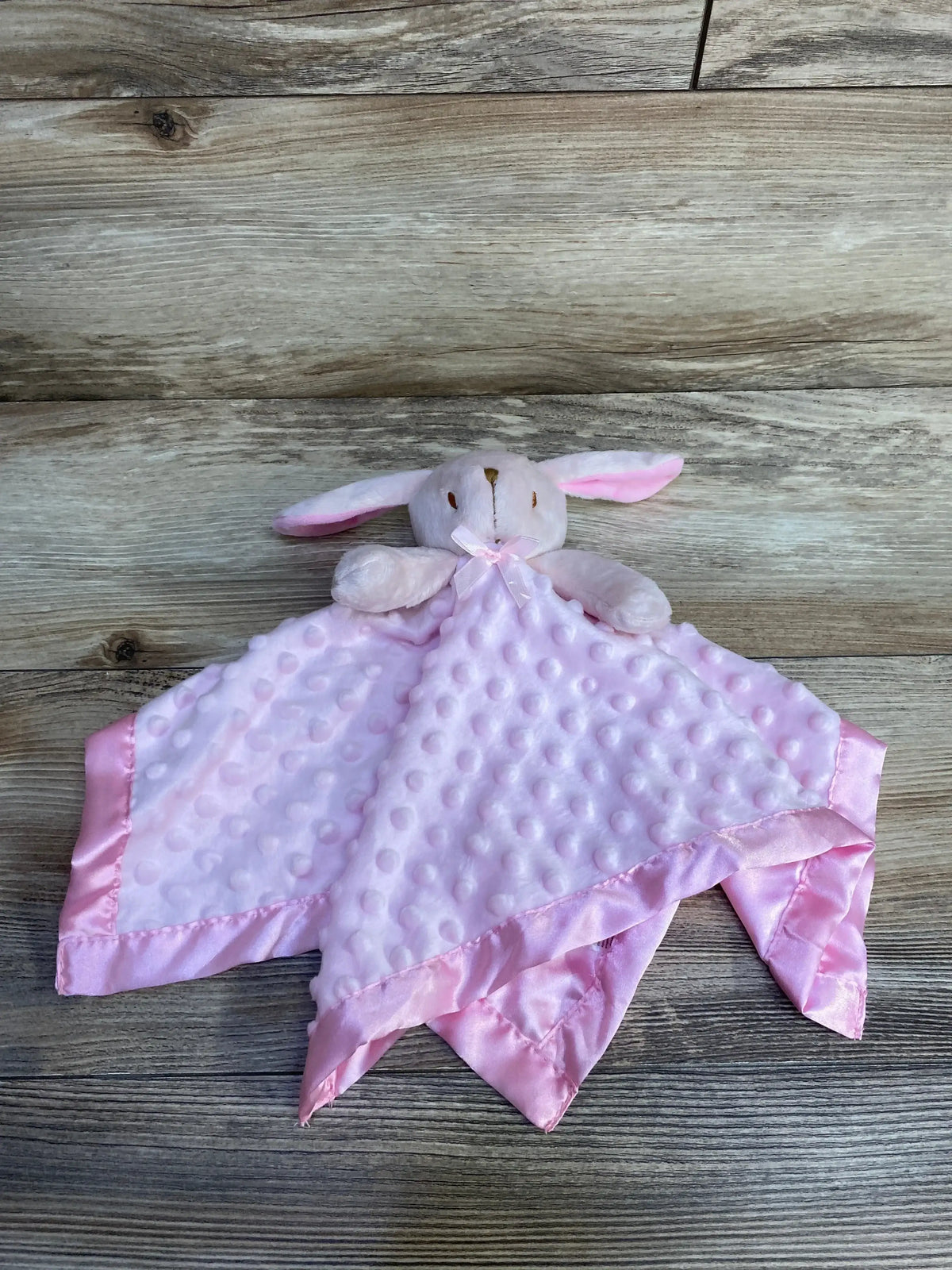 Top-down view of pink bunny lovey security blanket showing plush minky dot fabric and satin trim on wood background