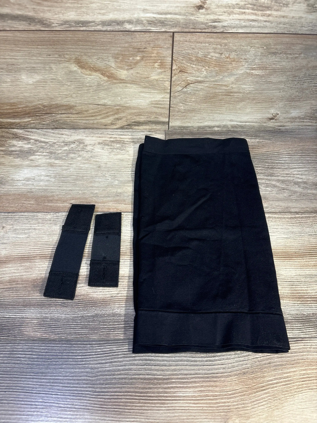 Flat lay of Kunindome maternity belly band and two black waist extenders highlighting stretch fabric on wood floor