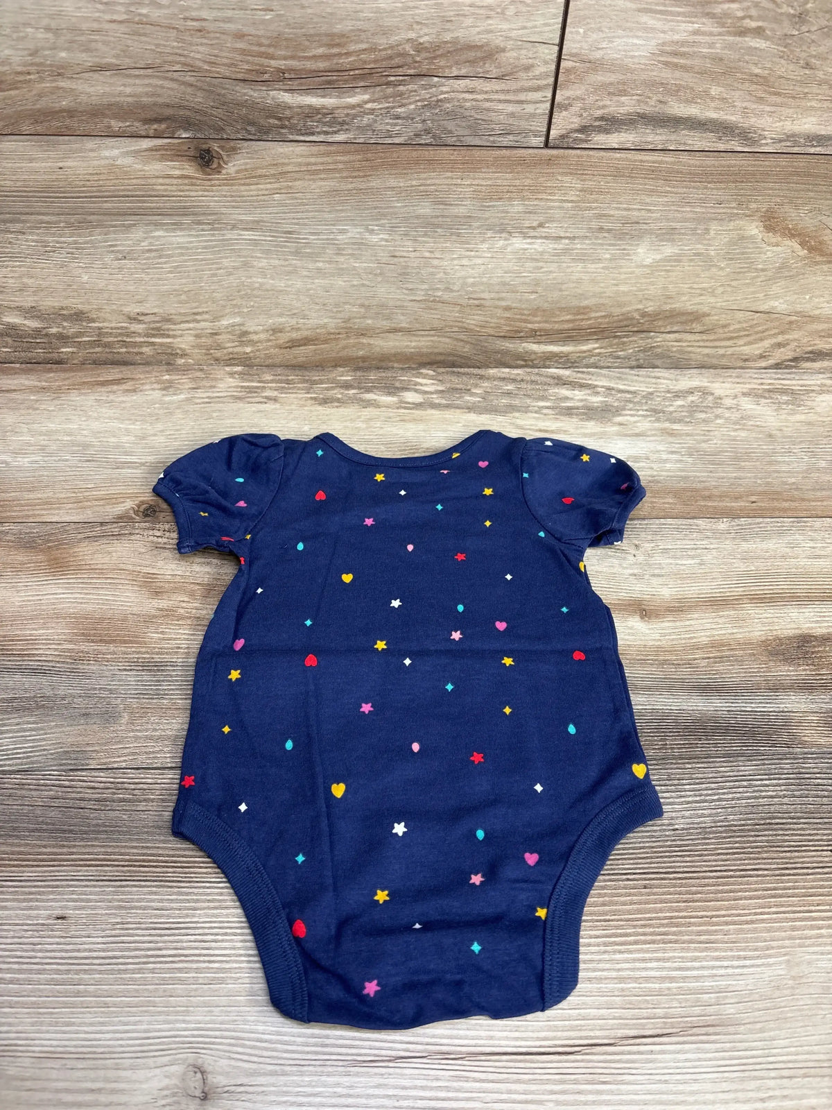 Navy blue baby onesie with short puff sleeves and multicolored hearts and stars pattern on wooden floor
