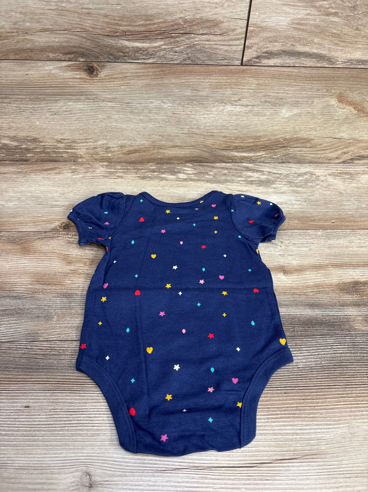 Navy blue baby onesie with short puff sleeves and multicolored hearts and stars pattern on wooden floor