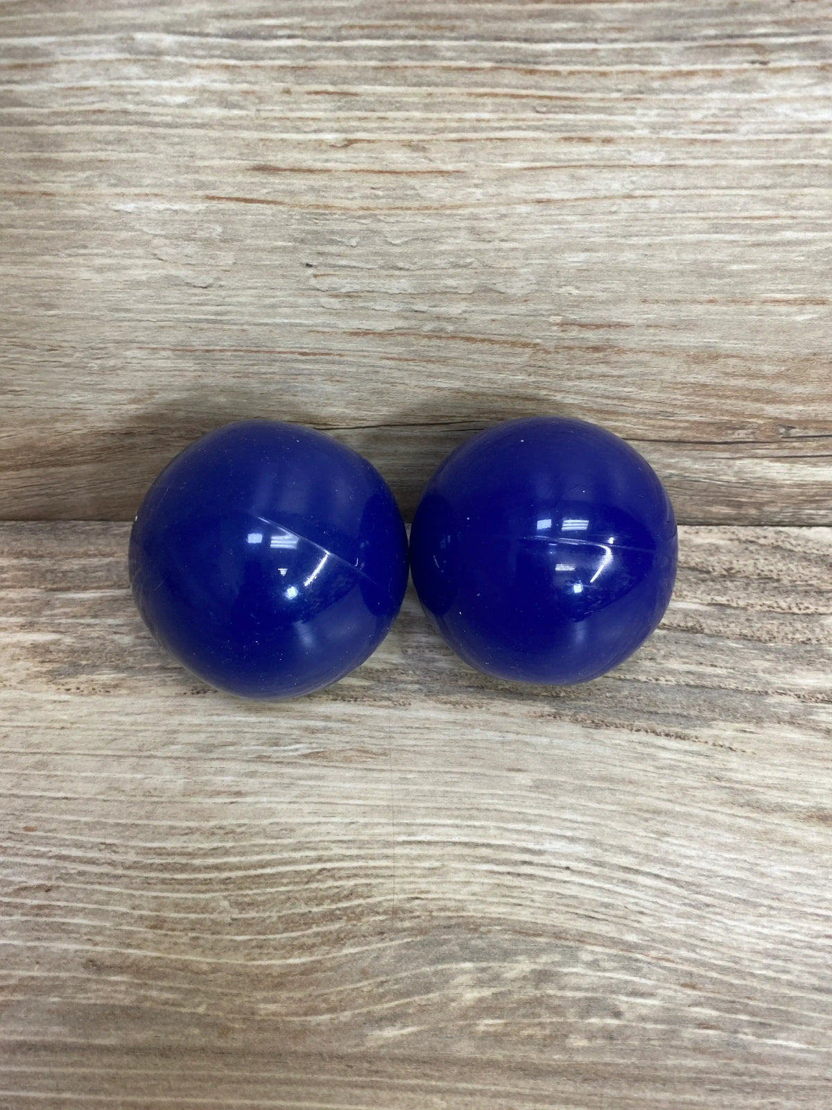 Front view of Lovevery Opposite Balls Blue showing two glossy blue plastic balls side by side on a light wood surface