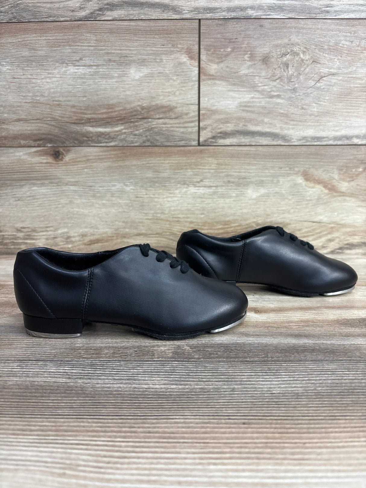 Pair of black leather tap dance shoes on wooden floor background