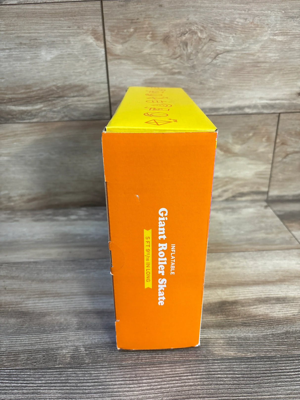 Box for inflatable giant roller skate toy, 5 feet long, on wood floor background