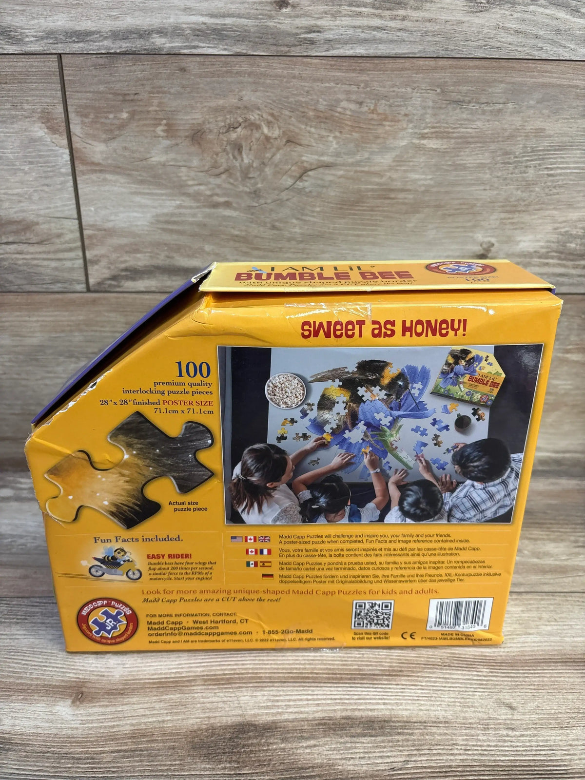 Back of Madd CAPP Lil' Bumble Bee 100-piece puzzle box showing headline Sweet as Honey and kids assembling pieces on wood