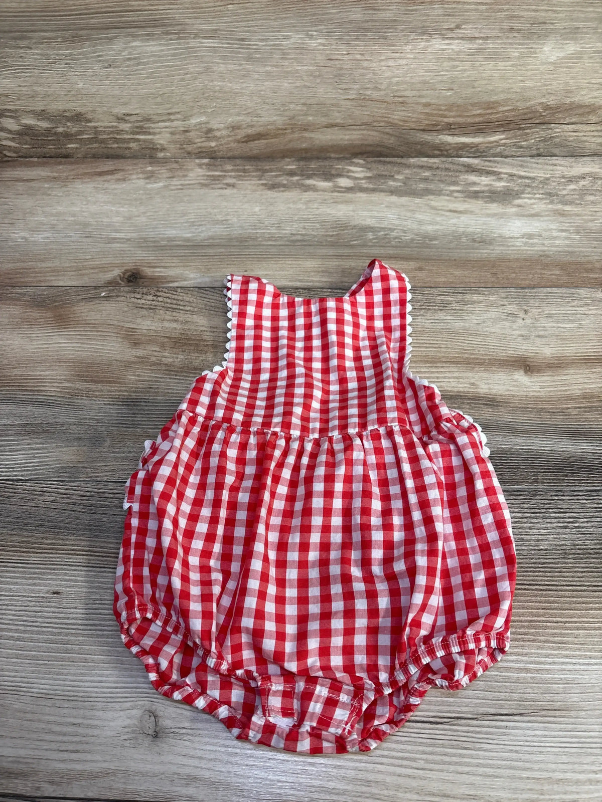 Top down view of red gingham ruffle bubble romper showing scalloped shoulder trim and elastic leg openings on wood background