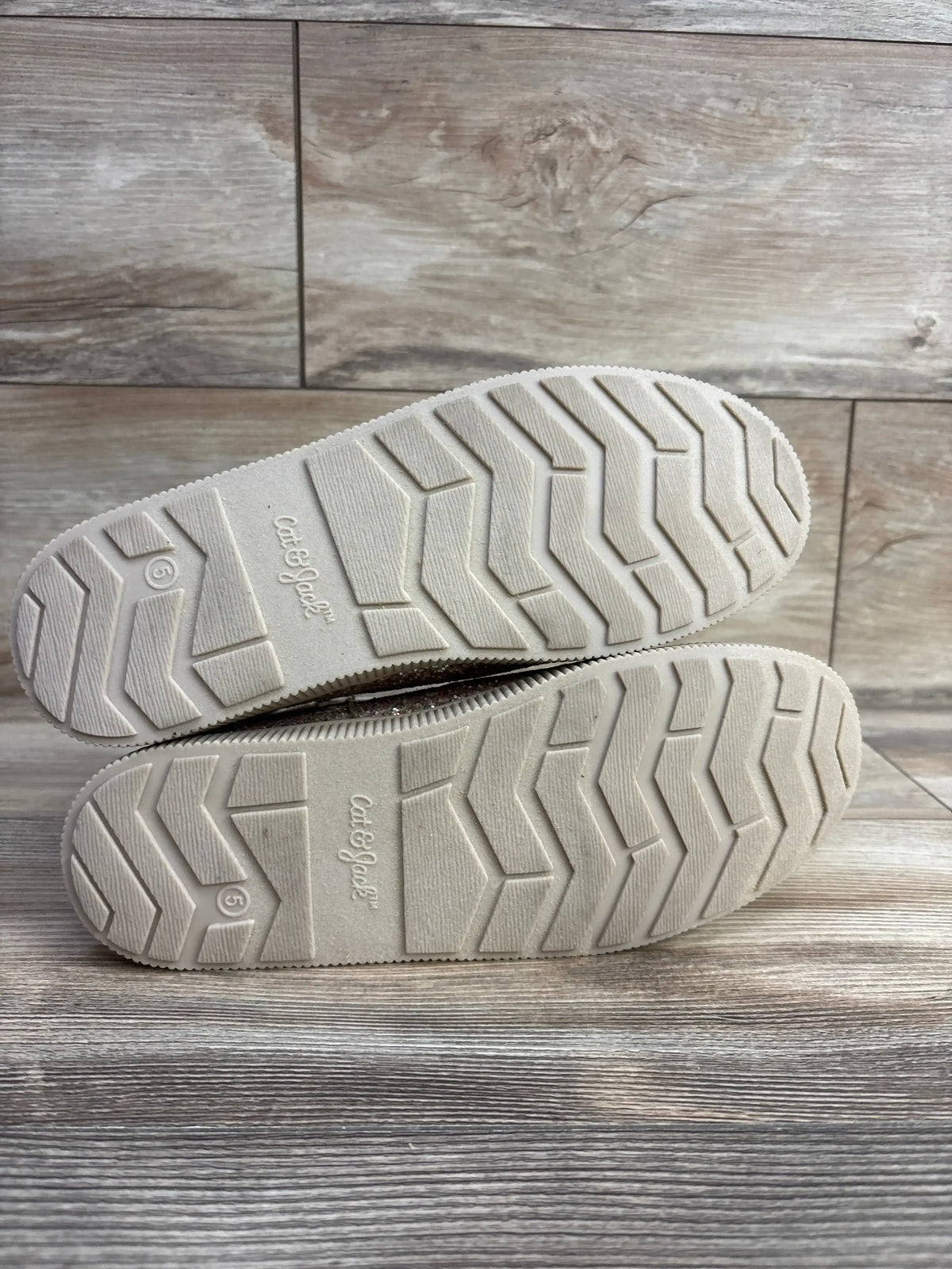 Bottom view of Cat & Jack Holland shearling-style kids boots showcasing white zigzag tread and visible size 5 marking on wood floor