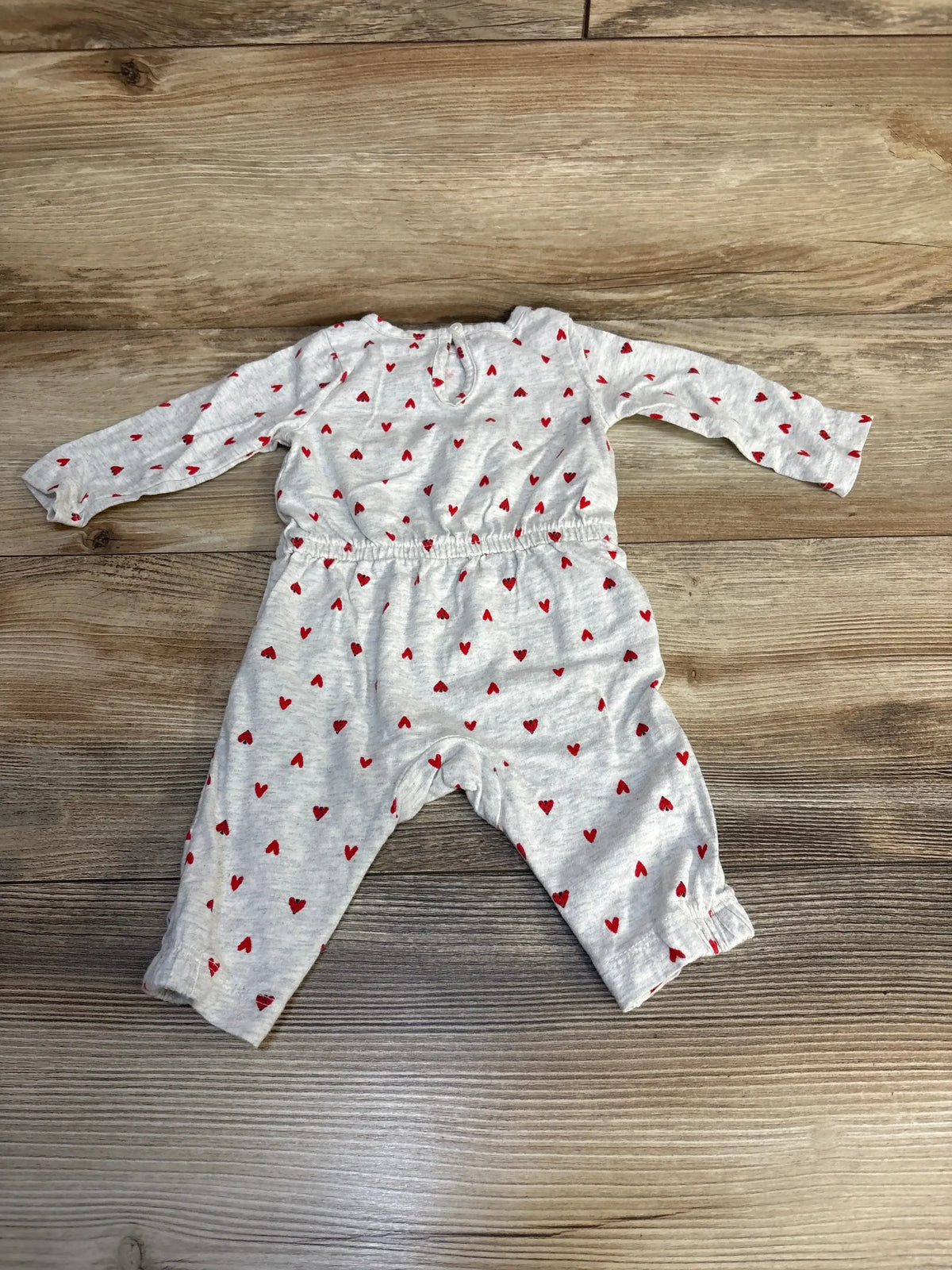 Flat lay of Just One You grey baby coverall size 3M showing red heart print, long sleeves, and elastic waist on wood floor