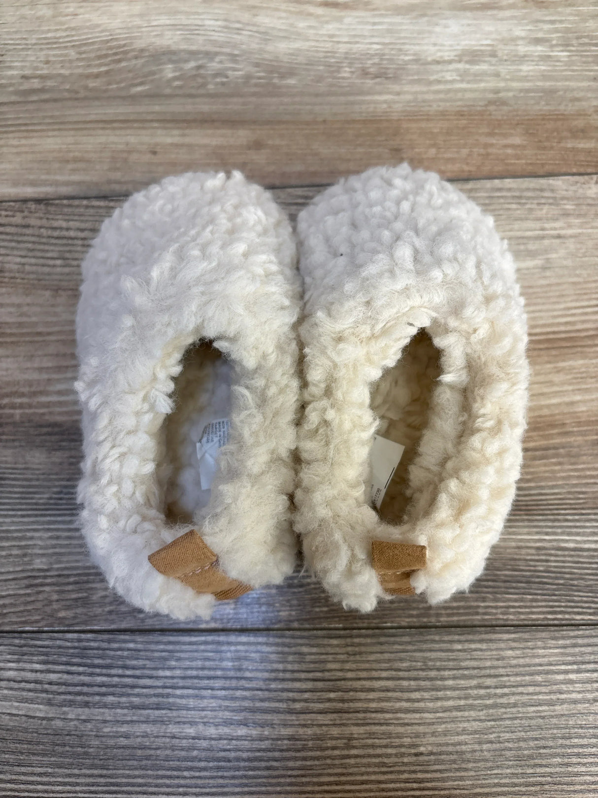 Fuzzy cream baby booties with soft soles on wooden background, cozy infant footwear