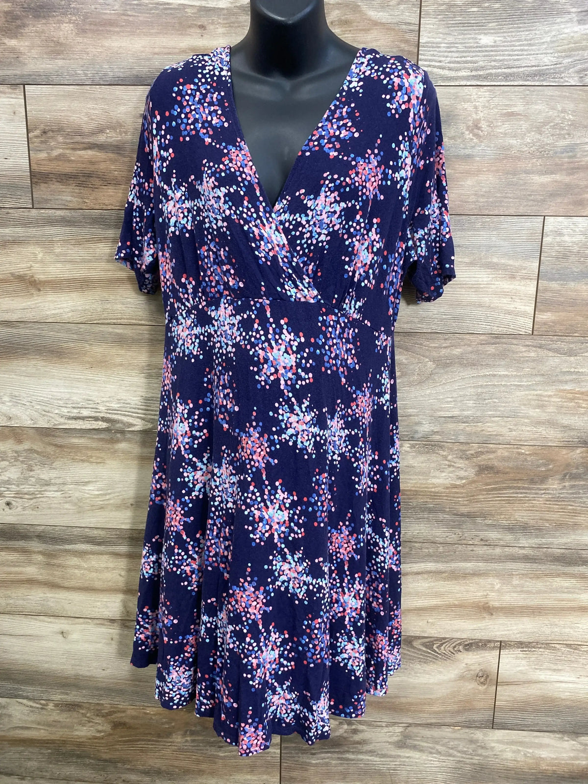 Front view of navy maternity dress with V-neck wrap, empire waist and multicolor starburst print on mannequin on wood wall