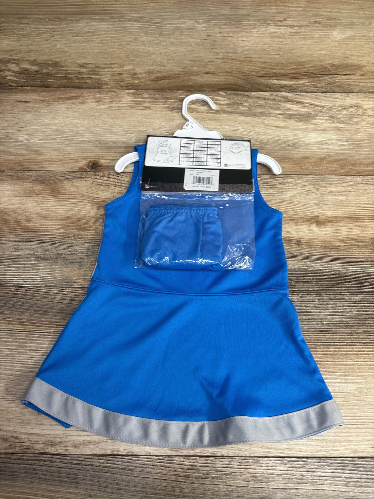 Blue sleeveless toddler dress with silver hem and matching shorts on white hanger on wooden floor