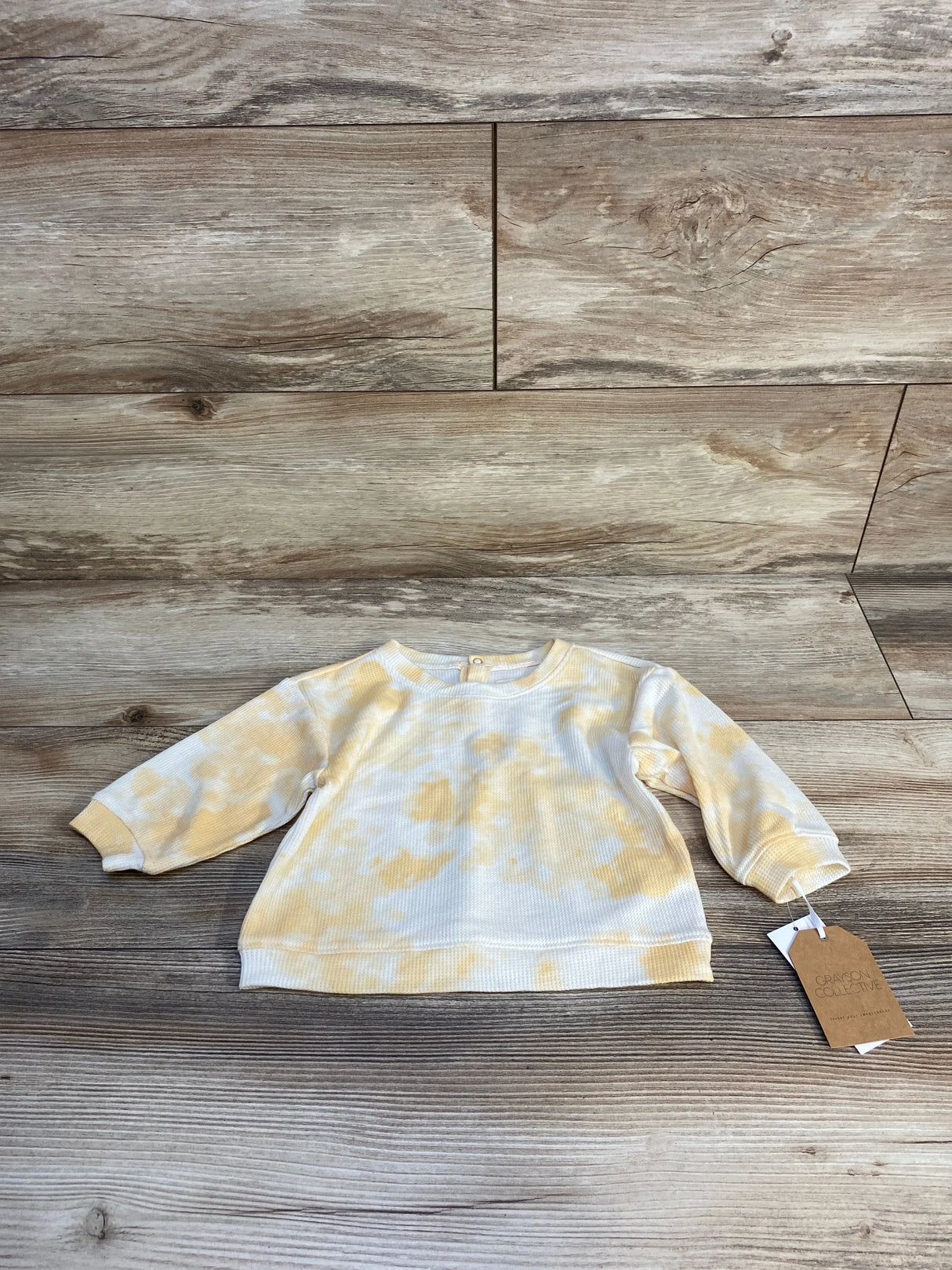 Yellow and white tie-dye long sleeve baby shirt on wood background with product tag