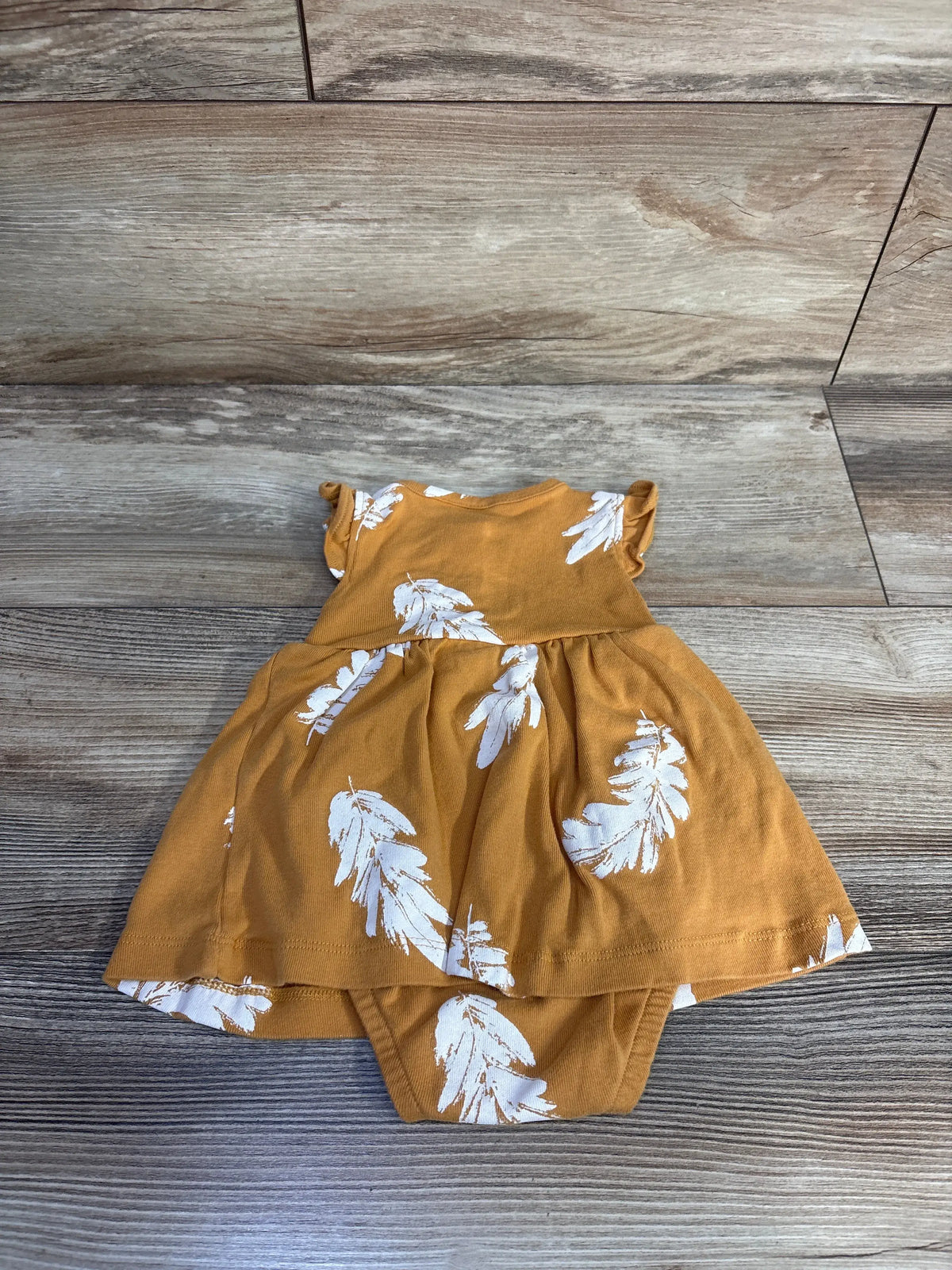 Front view of Carter’s yellow Henley bodysuit dress showcasing its A-line silhouette and white feather print on a wood-look floor