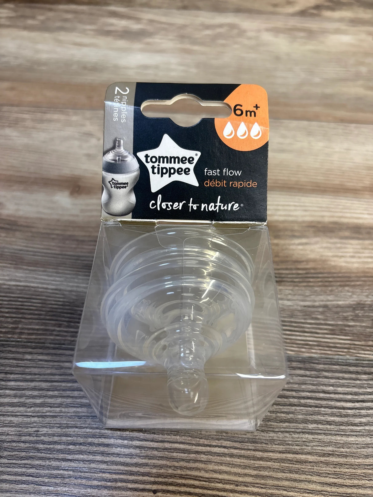 Front view of Tommee Tippee Closer to Nature fast-flow baby bottle nipples 2-pack showing clear silicone nipples in transparent box on wood surface