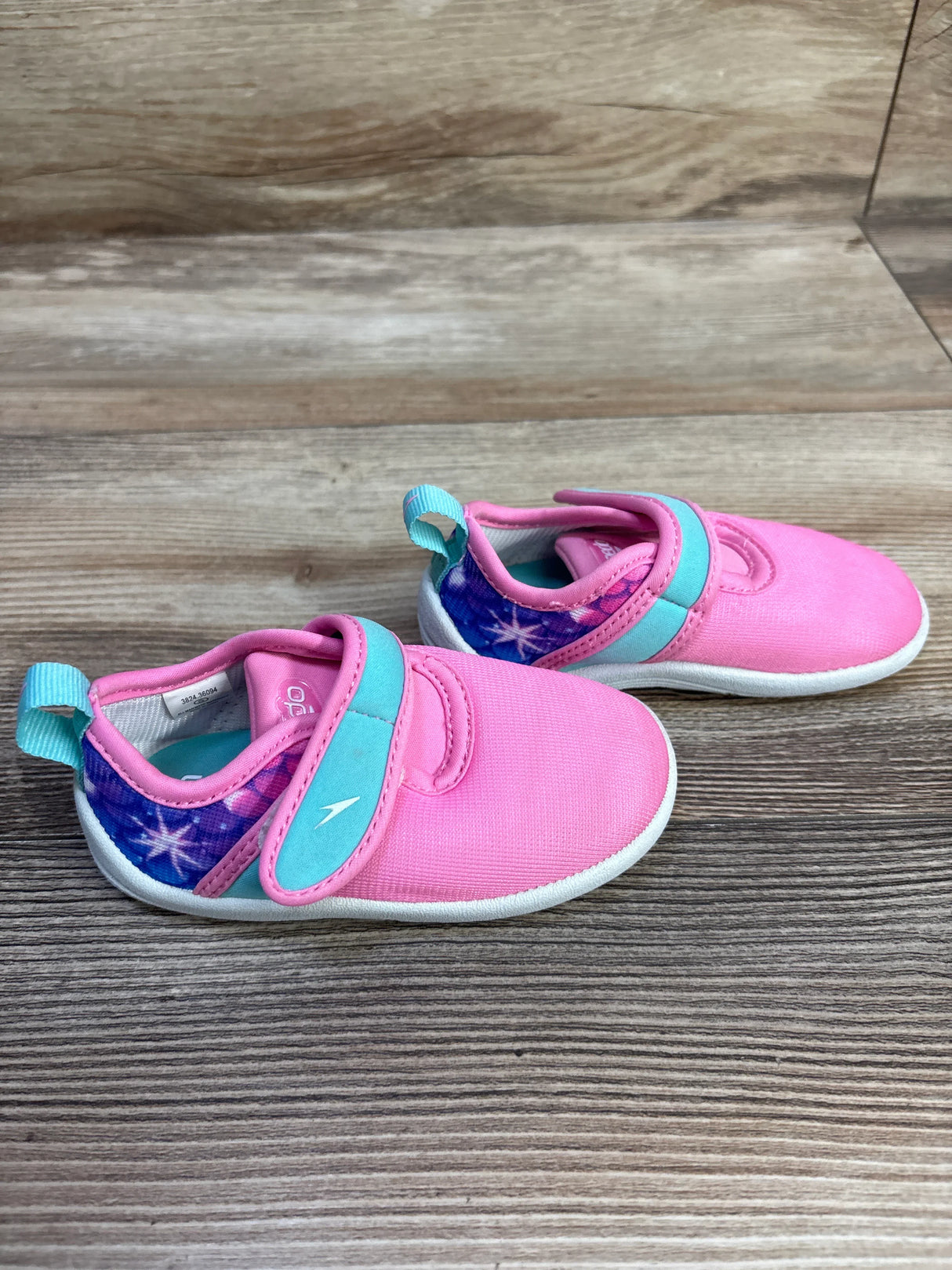 Angled view of Speedo Shore Explorer water shoes, pink with turquoise Velcro strap, star-print heel on wood background