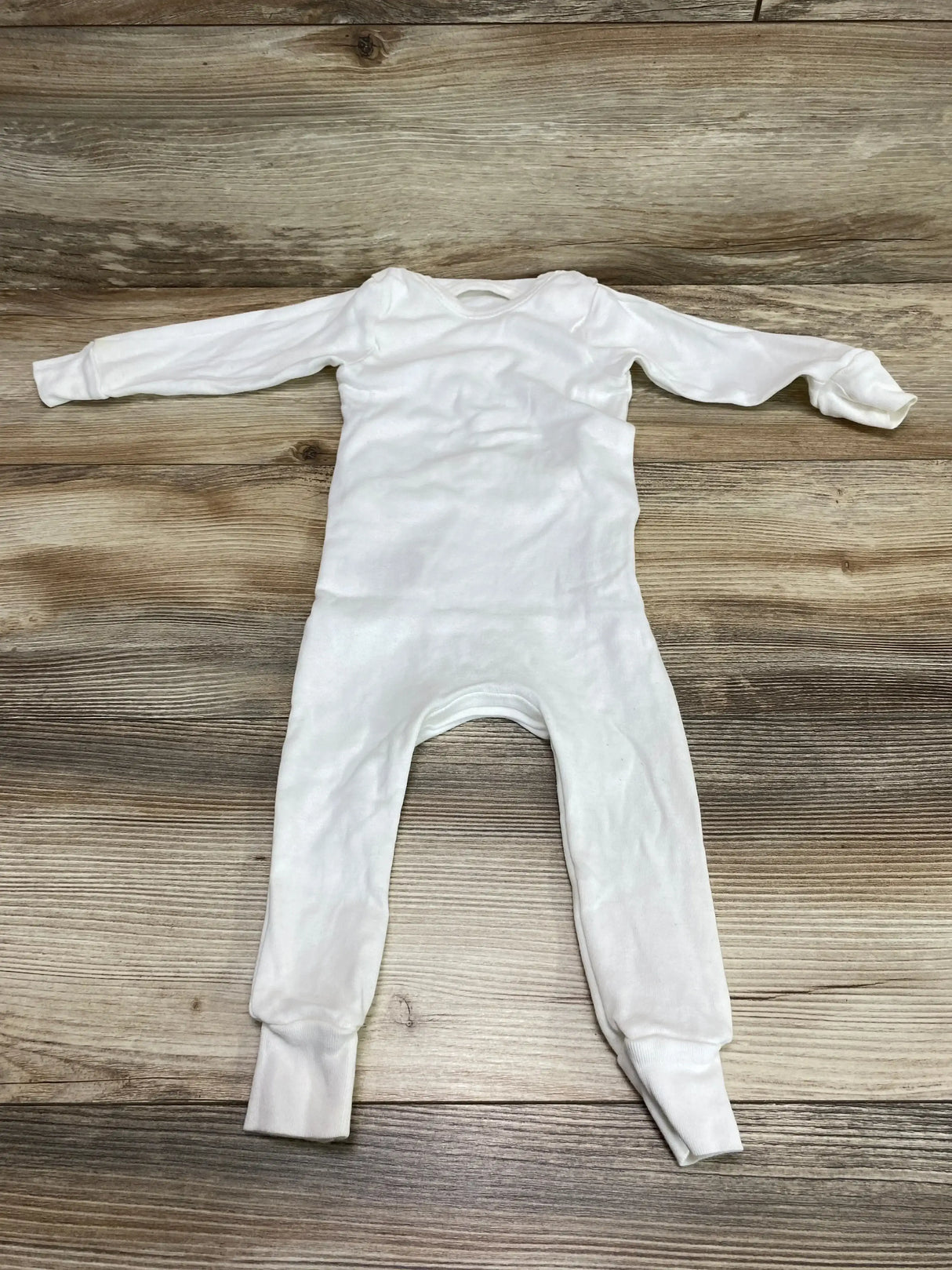 Flat lay of Mustela white baby onesie (6-12 months) showing long sleeves and cuffed legs on wood background