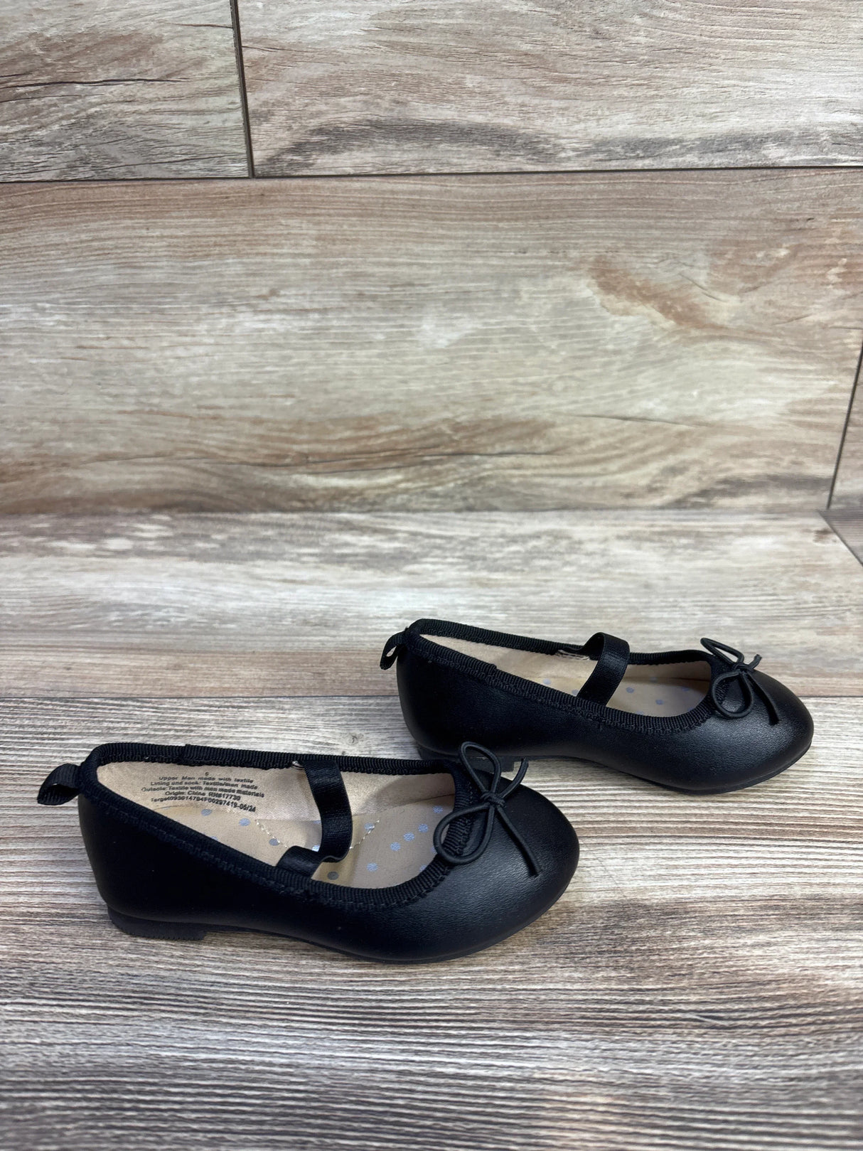Side view of Cat and Jack Nora slip on ballet flats, toddler size 6C, showing elastic strap and bow on light wood background