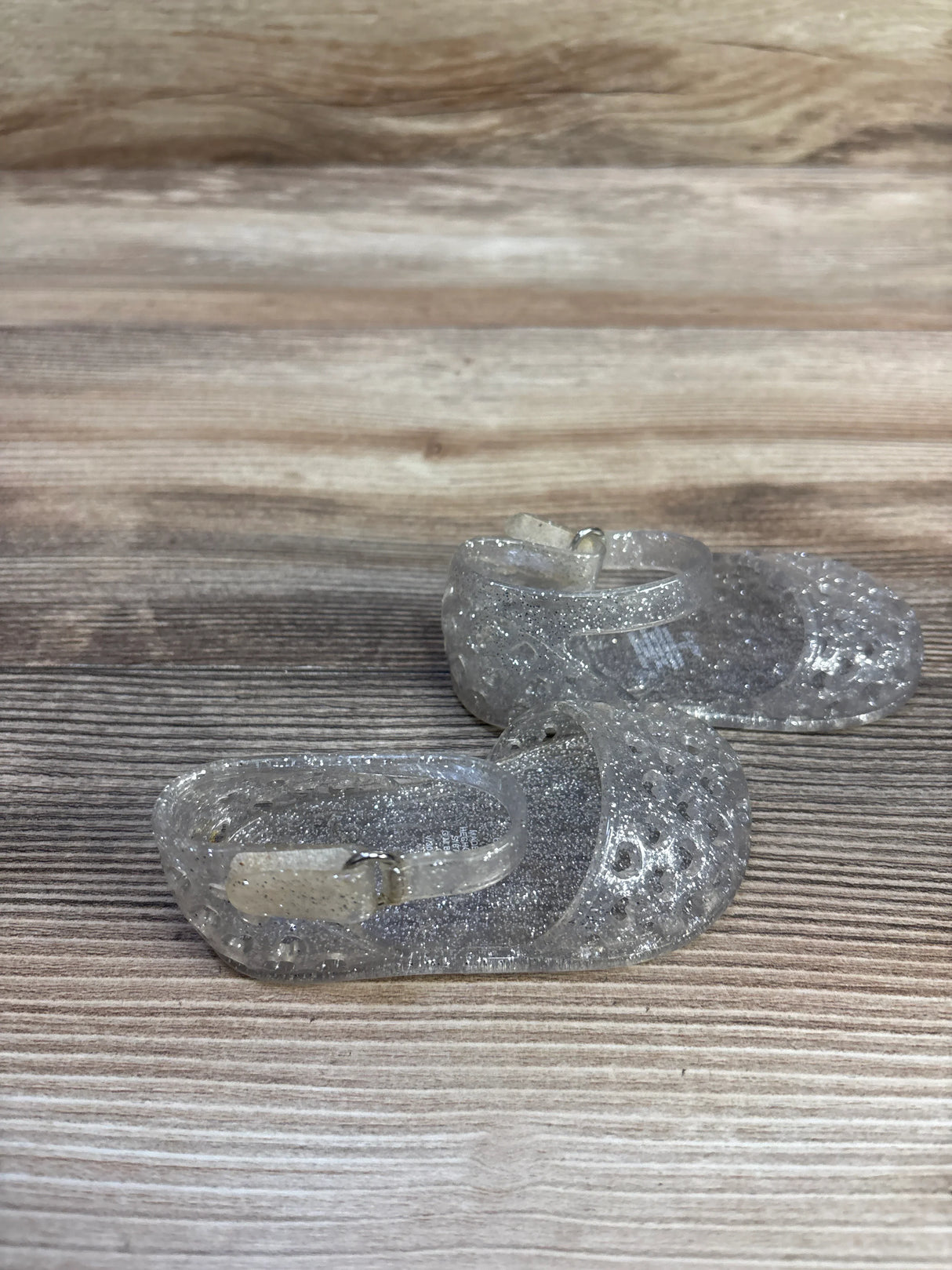 Front view of clear glitter toddler jelly sandals size 3C showcasing ankle strap buckle and perforated toe on wood
