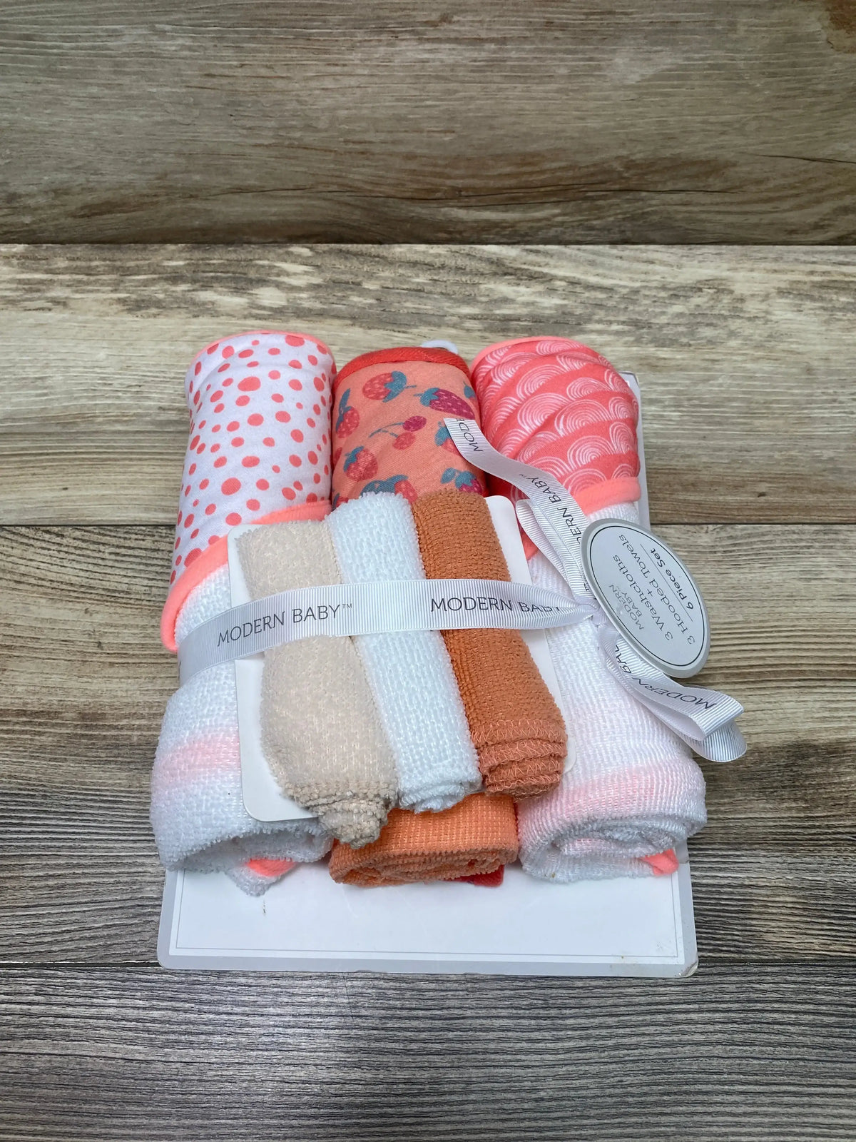 Front view of Modern Baby 6-piece peach hooded towel and washcloth set with patterned hood and terry washcloths on wood
