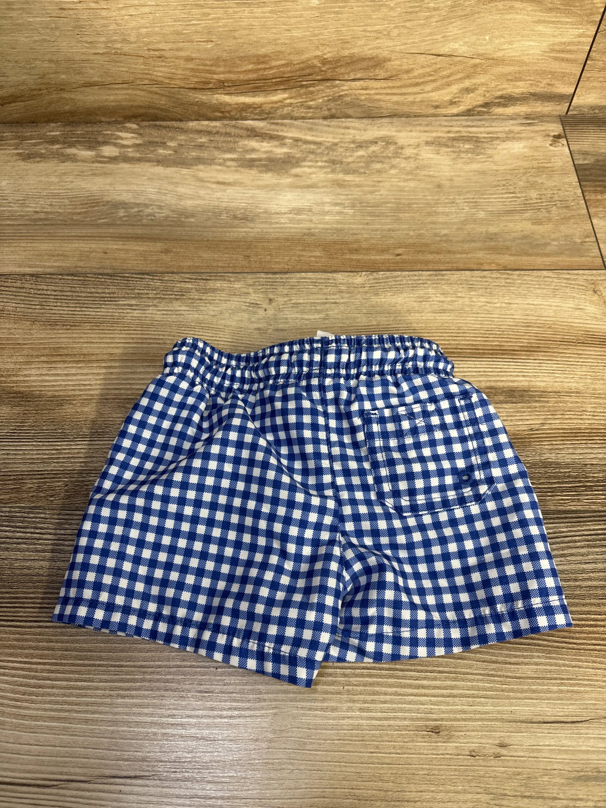 Front view of Cat & Jack blue swim trunks showcasing a white gingham pattern and elastic waistband on a wood surface