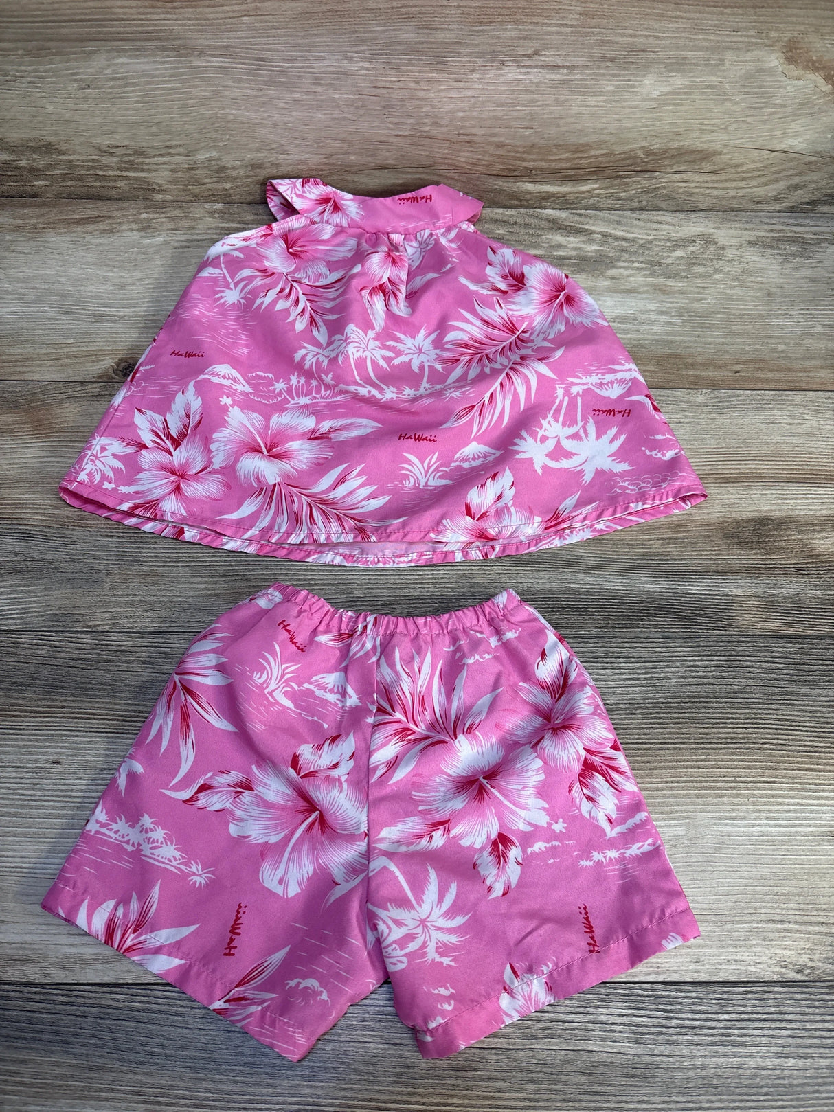 Pink floral Hawaiian print toddler outfit with sleeveless top and shorts on wood background