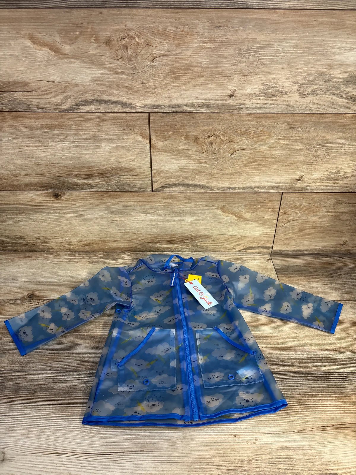 Blue clear rain jacket for toddlers with a white cloud print, laid flat on wood background.