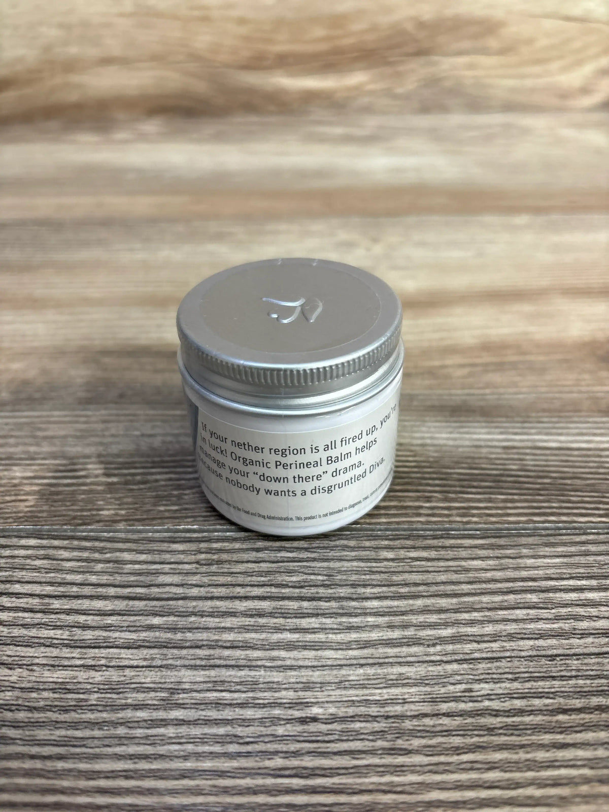 Front view of NEW Earth Mama Organic Perineal Balm 2oz showcasing its silver lid on a wood grain surface