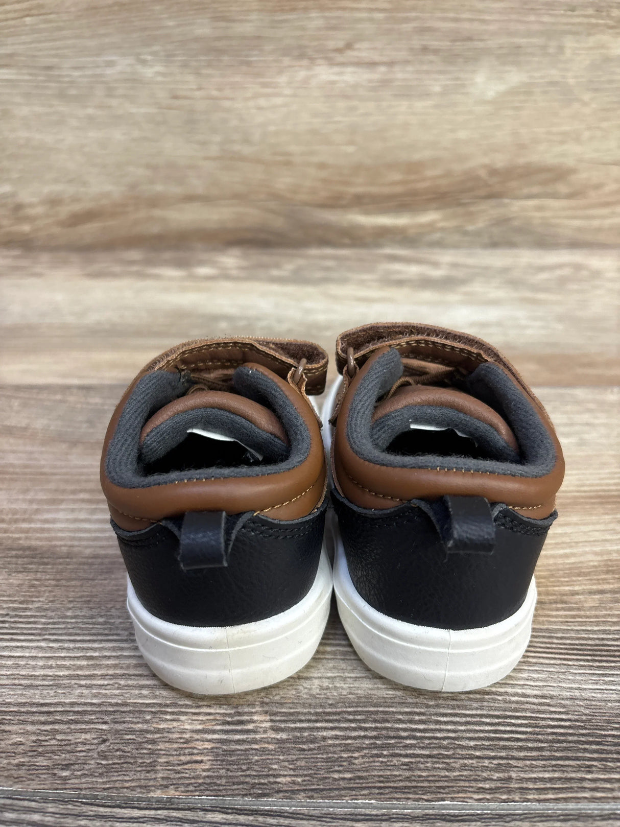 Rear view of Carter's toddler brown and black casual sneakers, size 6C, showing cushioned grey lining and white rubber soles on wood background