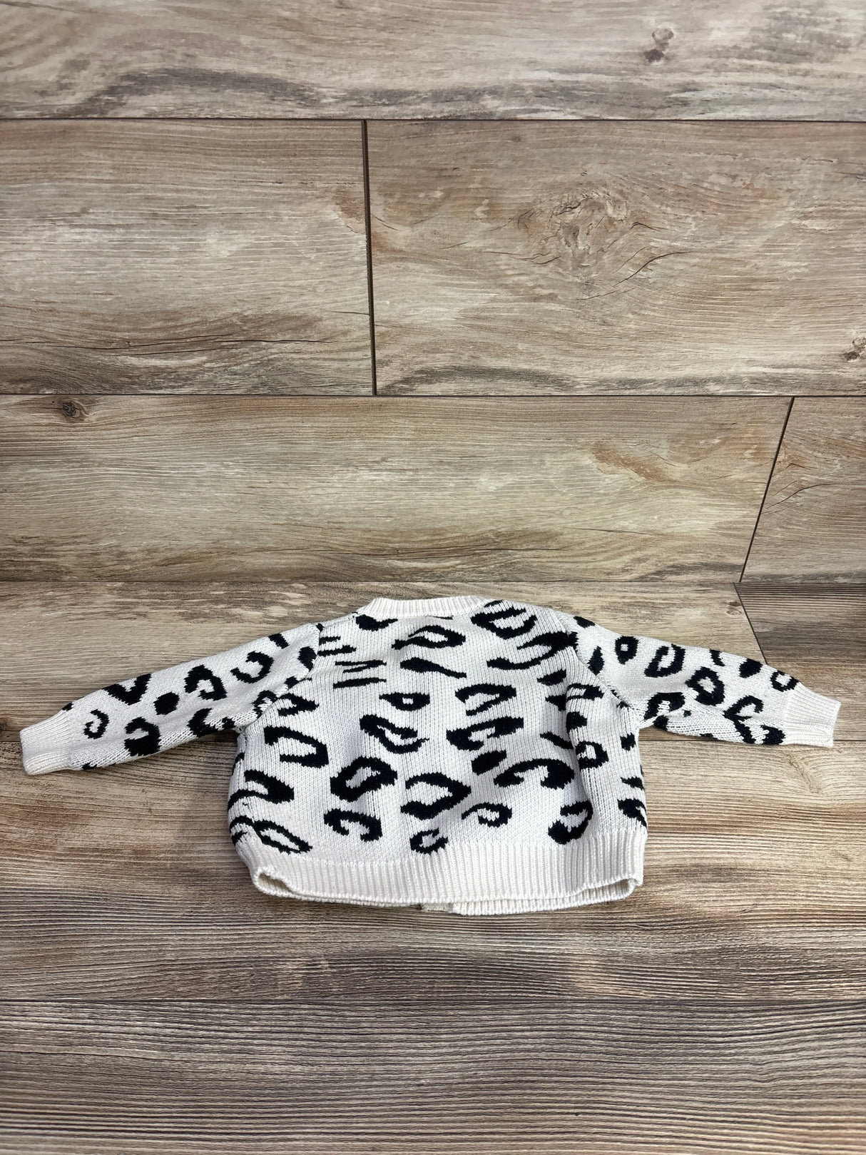 White and black animal print kids sweater laid flat on wooden floor