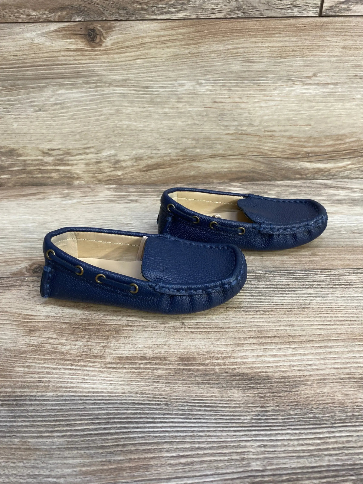 Angled side view of Janie & Jack navy toddler leather driving shoe showcasing pebbled leather, moccasin stitching, brass eyelets on wood background
