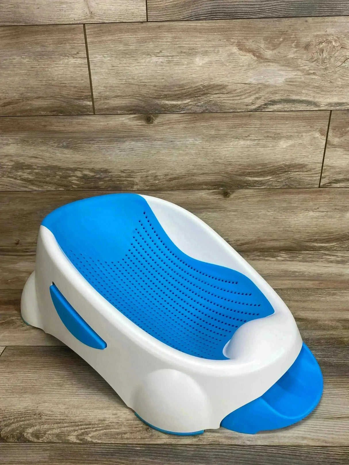Three-quarter view of Munchkin Clean Cradle baby bathtub with blue non-slip insert and contoured head support on wood floor