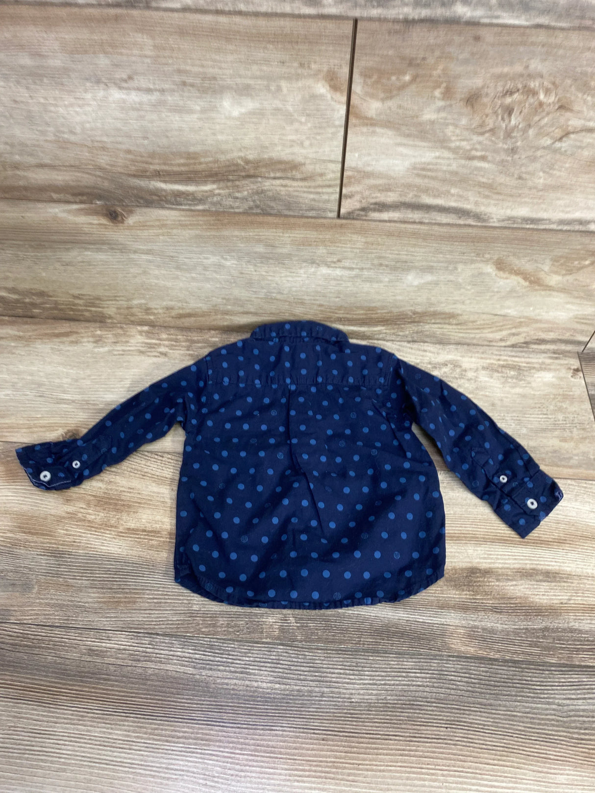 Navy blue long sleeve kids shirt with blue polka dots, button cuffs, on wood floor