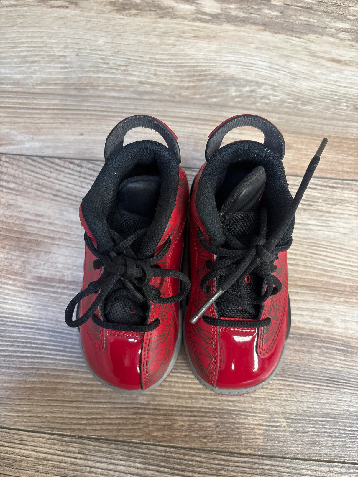 Top view of Air Jordan Dub Zero TD Toro Bravo toddler sneakers, size 6C, red patent upper with black laces on wood floor