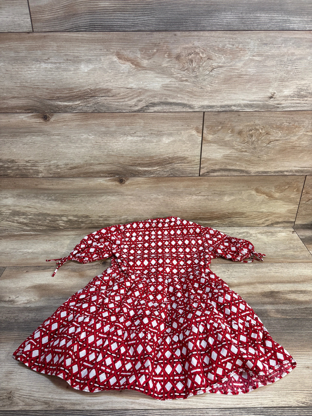 Top-down view of girls’ pocket dress size 5T showcasing red and white geometric print, puff sleeves with ties on wood floor