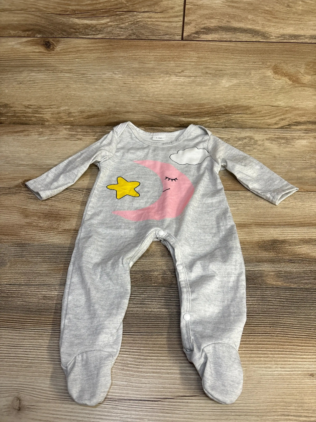 Front view of grey Moon and Star footed coverall with snap closures and moon, star, cloud design on wood floor