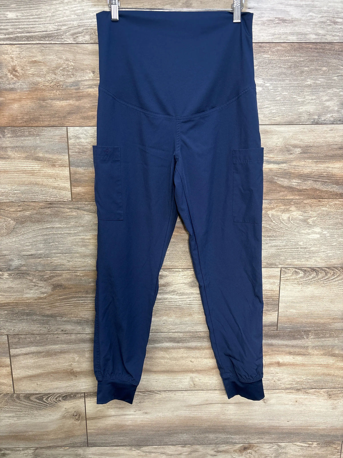 Front view of navy Medcouture maternity scrub pants showcasing full panel waistband and side pockets on a wood floor