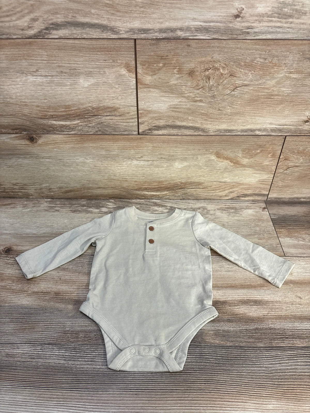 Front view of cream Telluride Henley bodysuit showcasing long sleeves, two button neckline, and snap closure on wood flooring