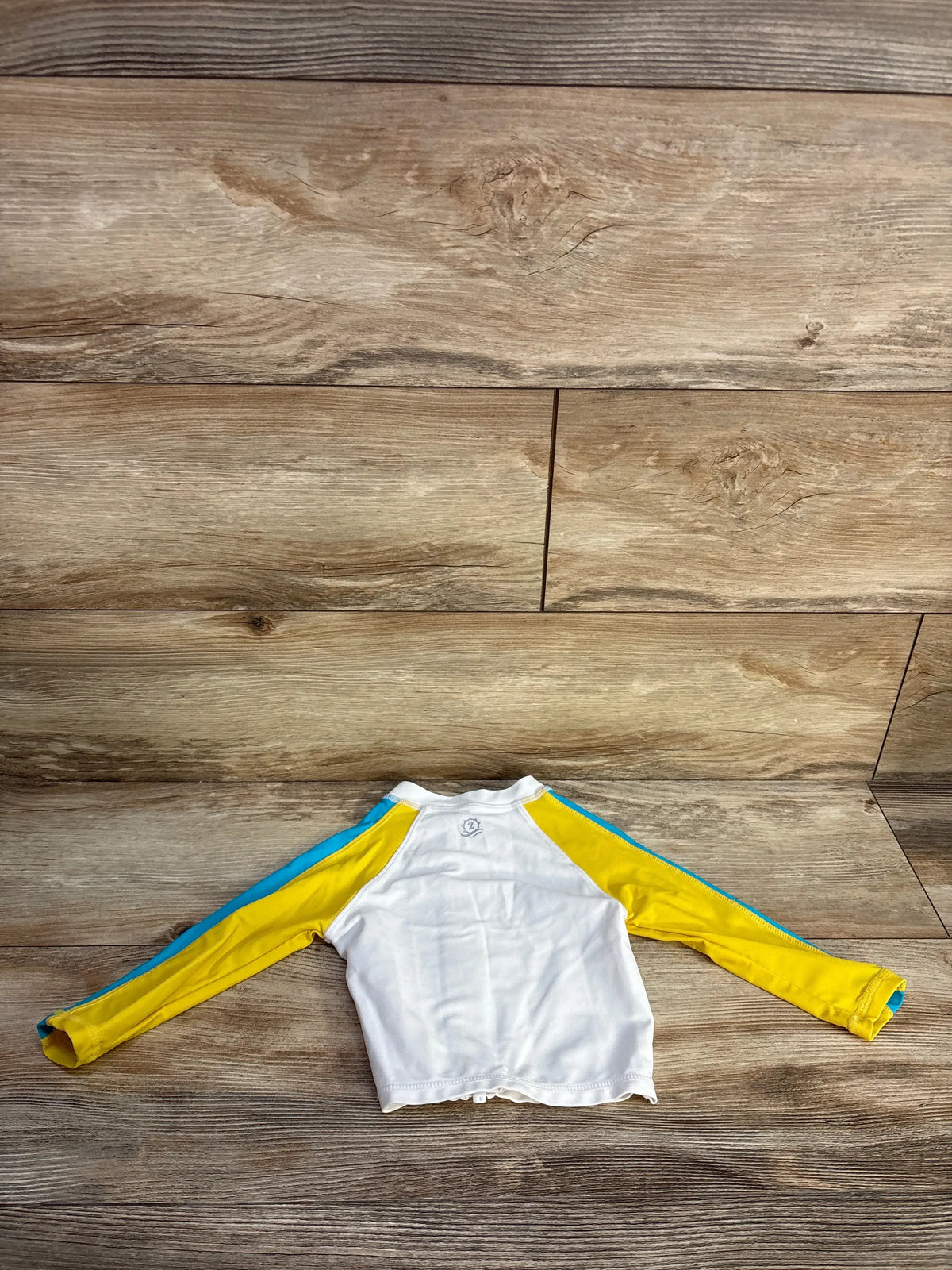 Flat view of SwimZip white long-sleeve zip-up rash guard shirt, size 12m, with yellow sleeves and blue trim on wood floor