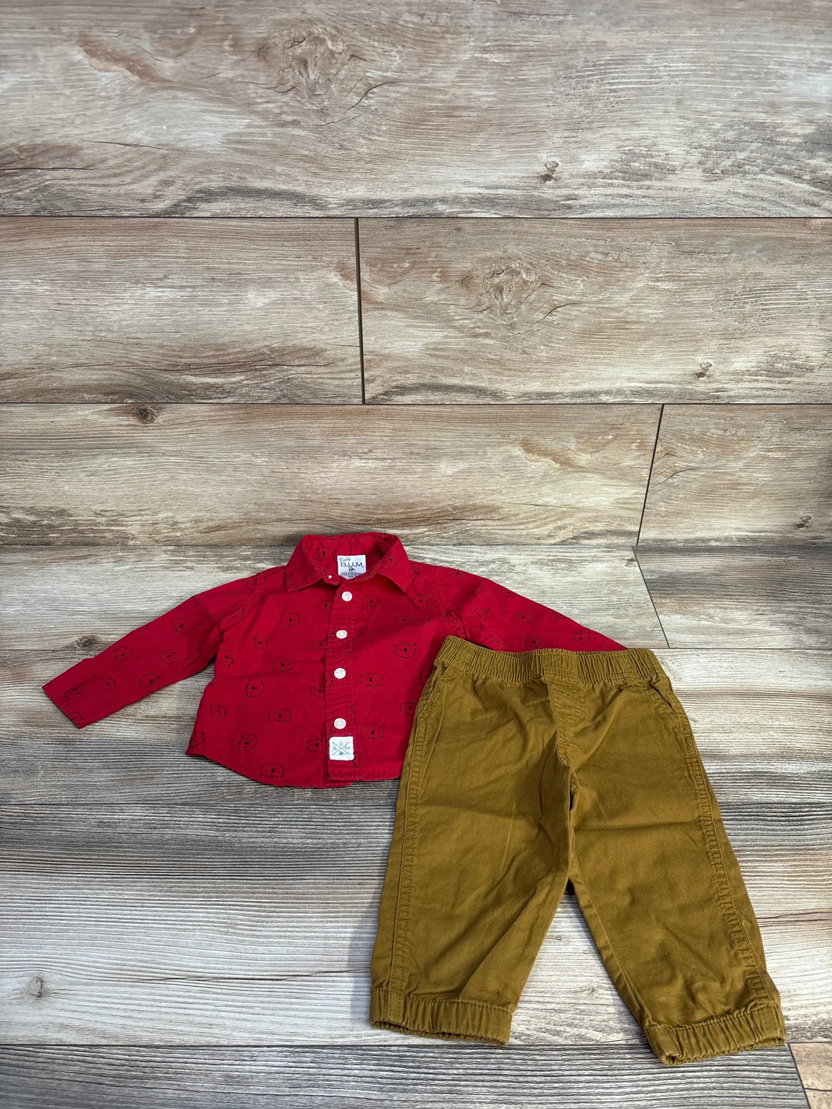 Top view of Baby B.U.M 2pc Button-Up Shirt & Pants Set showcasing red patterned shirt and elastic-cuff pants on wood-look floor