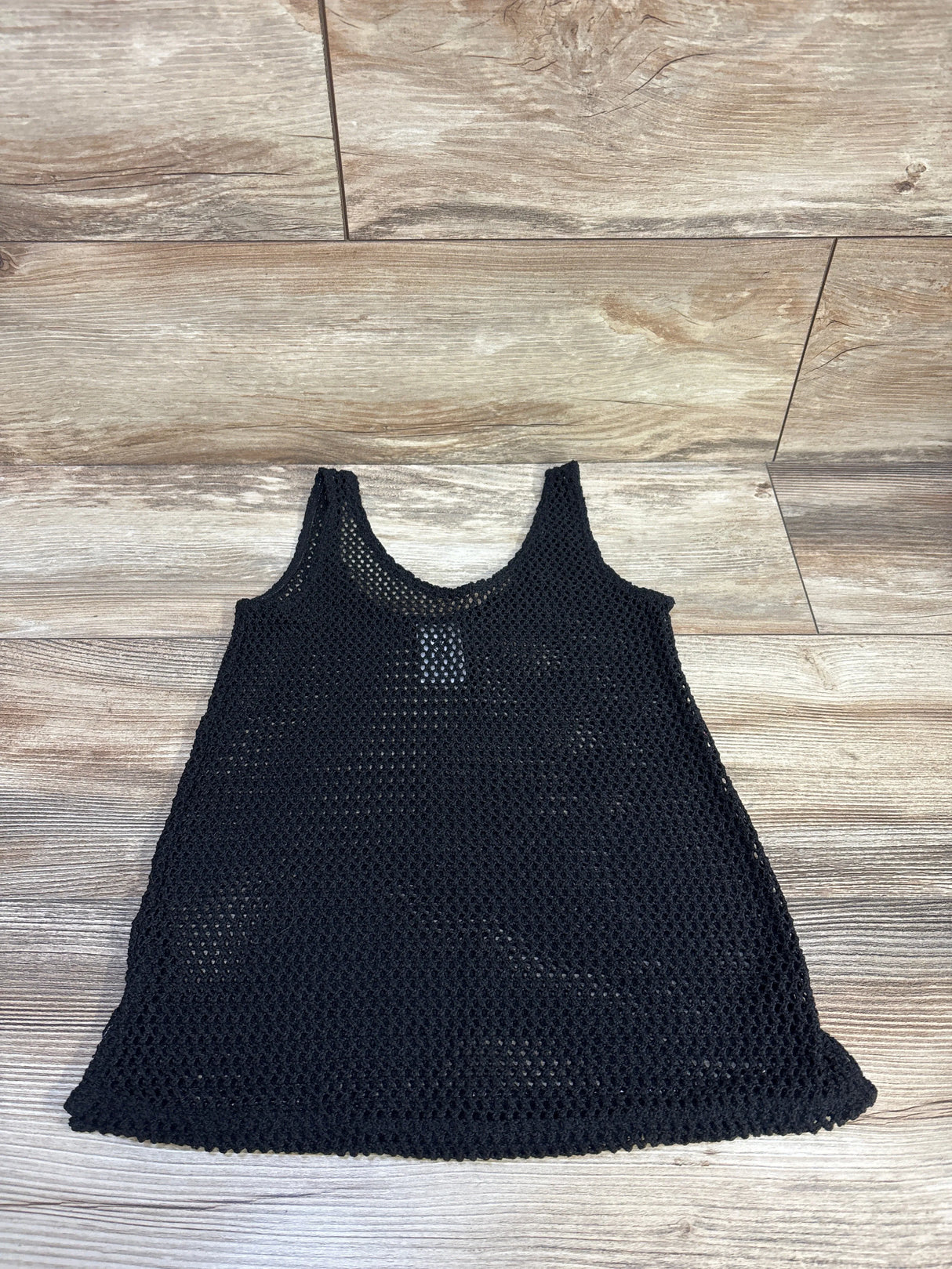 Flat lay of black mesh swim cover-up size 4/5T showing sleeveless open-knit fabric on light wood floor