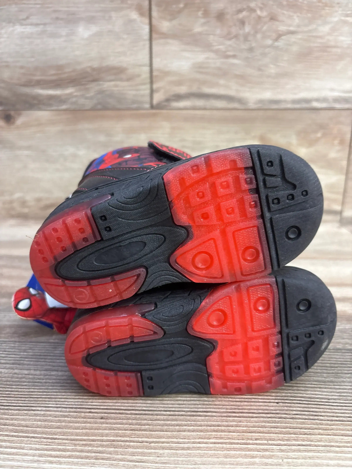 Bottom view of Marvel Spider-Man toddler winter boots showcasing red translucent rubber soles on wood floor background