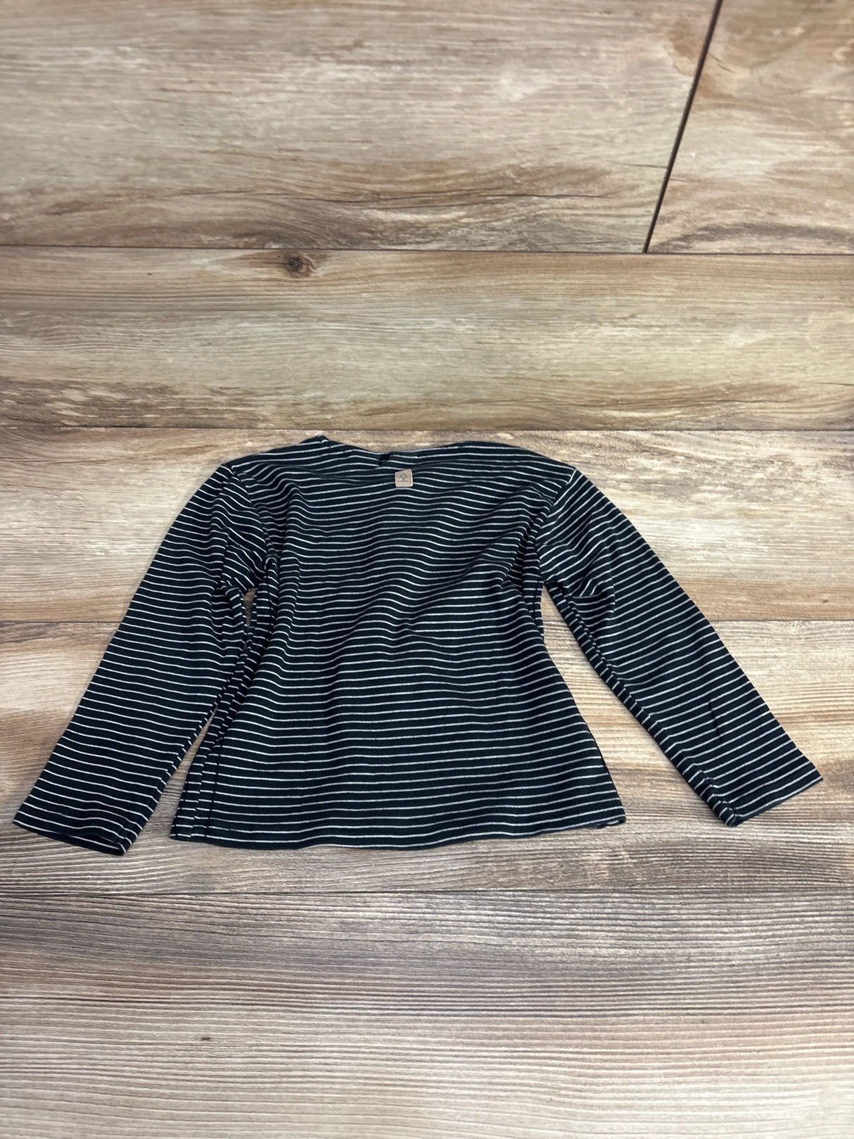 Black and white striped long-sleeve toddler shirt laid flat on wooden floor