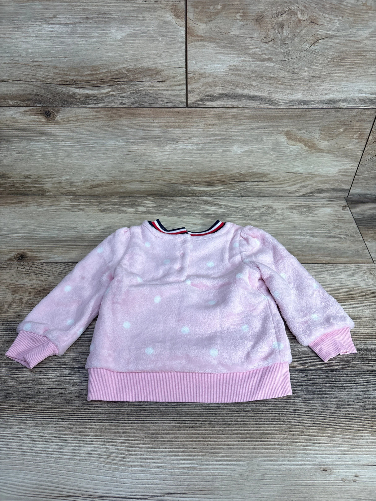 Pink fleece toddler sweater with white polka dots and ribbed cuffs, laid flat on wood