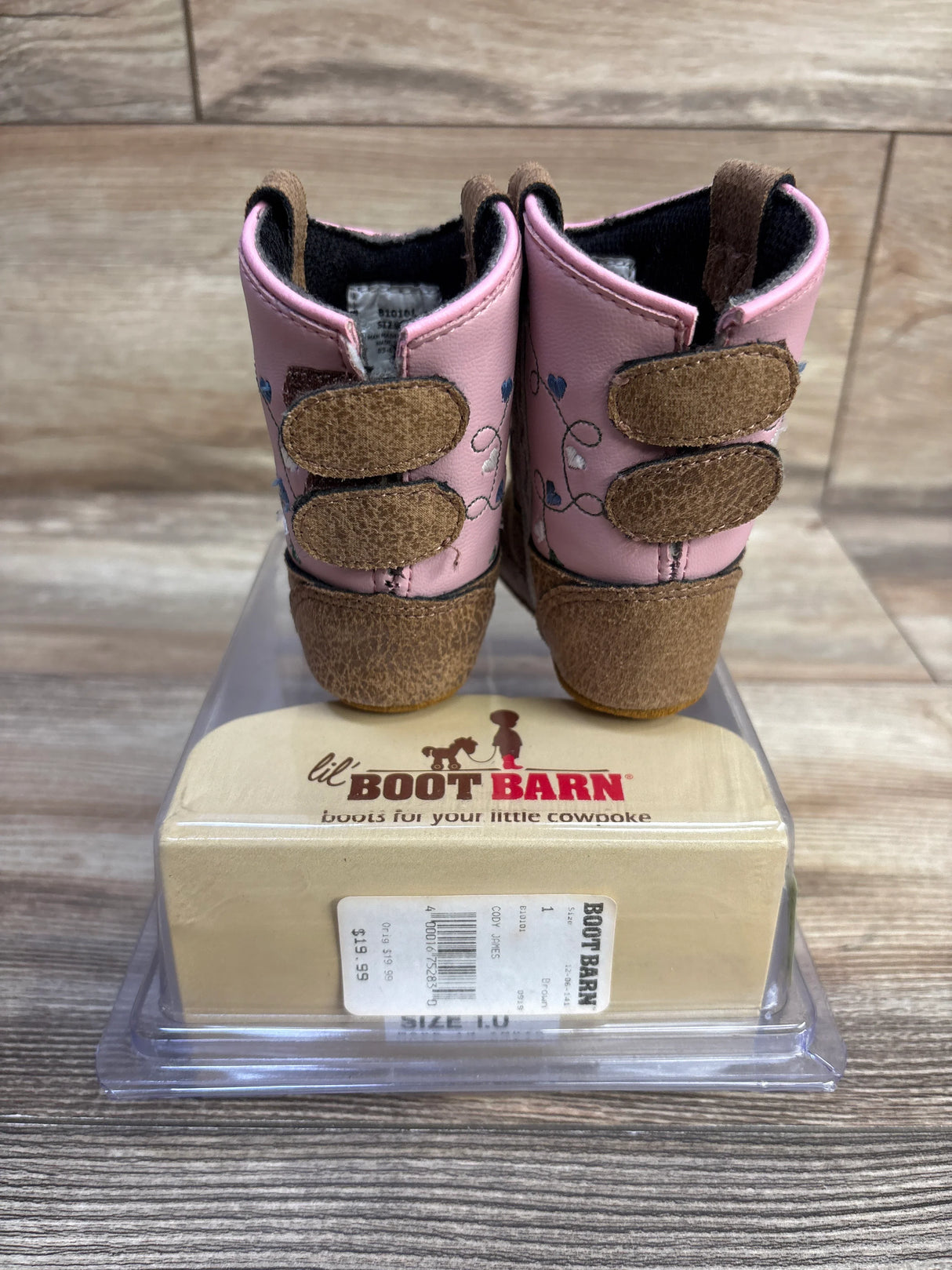 Rear view of pink Old West Poppets toddler cowboy boots showing brown suede heels, two Velcro straps and heart embroidery on a wooden floor