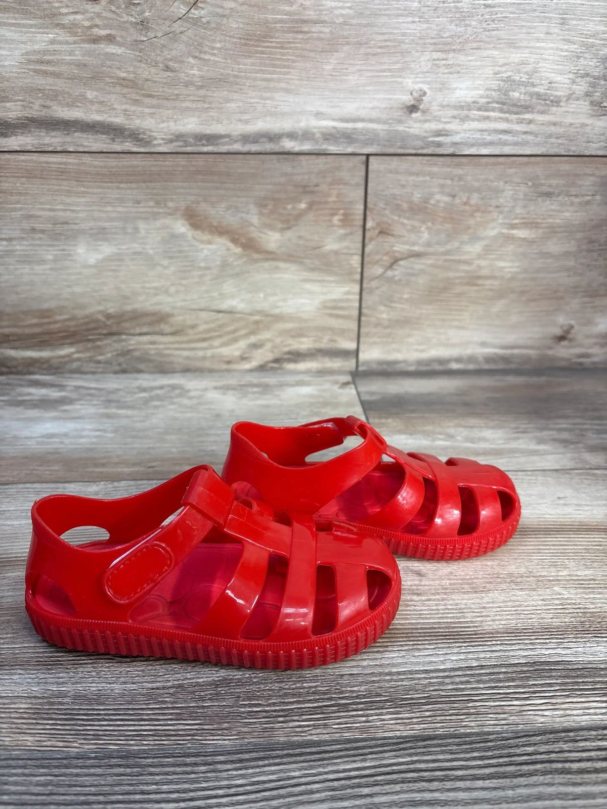 Front and side view of red Jelly Fisherman Sandals in size 8/9C showcasing hook and loop closure with a wood-grain background
