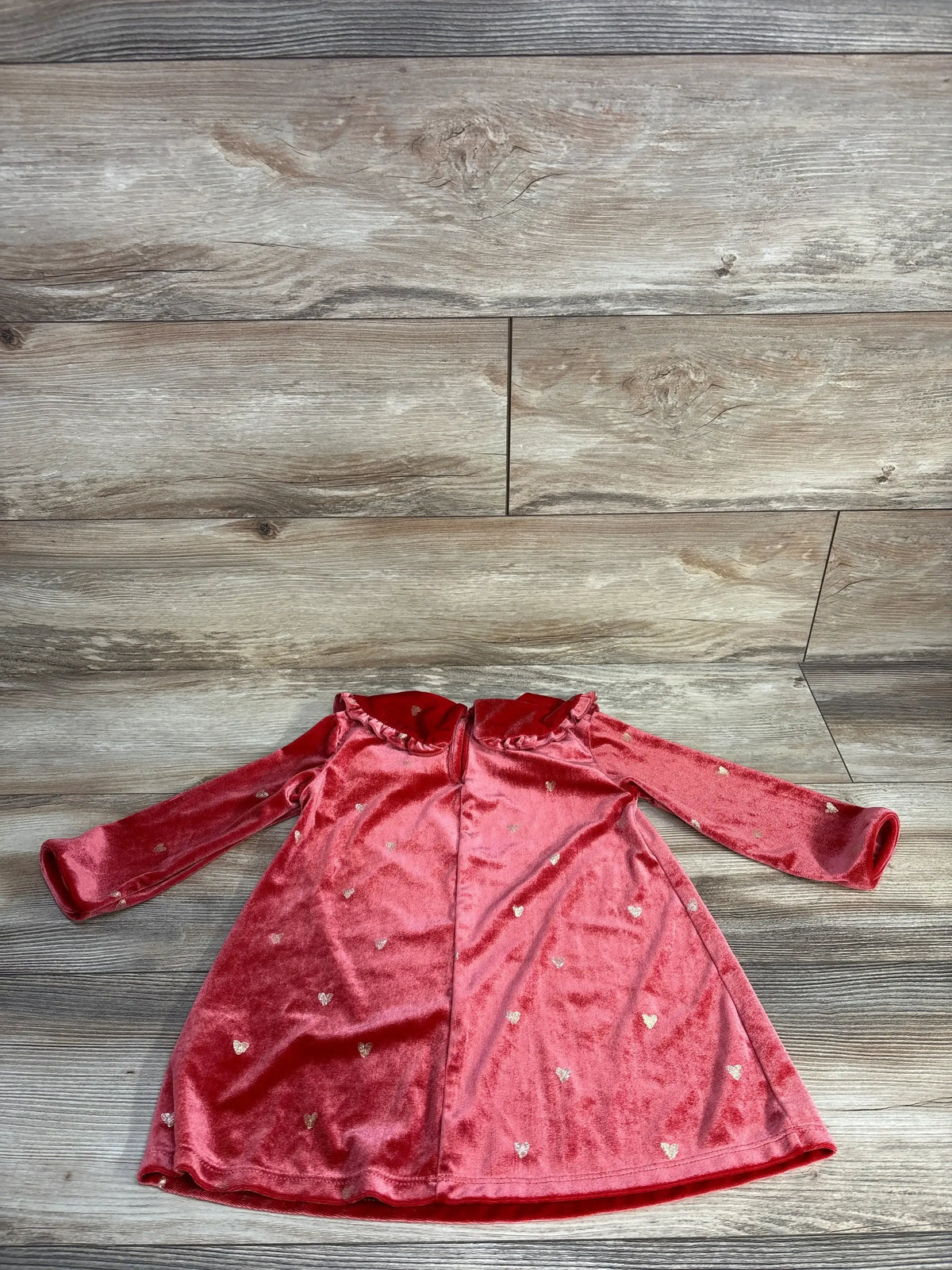 Front flat-lay of H&M red velvet toddler dress (2T) showing long sleeves, ruffled collar, and small gold hearts on a wooden floor
